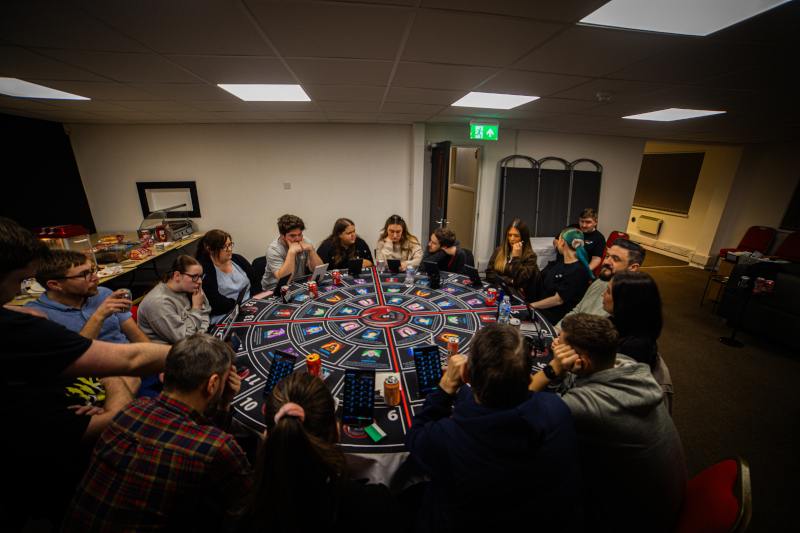 16 players sitting at a round table waiting to get started playing the final of the Conspiracy LIVE league